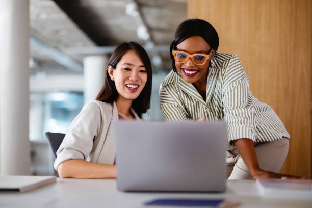 Two professional women discussing work on a laptop, demonstrating teamwork and collaboration in a modern office setting.